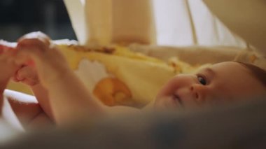 Child in the cradle. Authentic Close Up Footage of a Cute Newborn Baby Lying on the Back in Child Crib. Playful Portrait of a Caucasian Neonate Toddler. Concept of Childhood, New Life and Parenthood.