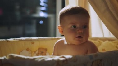 Baby care, first skills, learning to sit. Happy baby sitting in the crib. Baby sitting in crib in night. Baby sitting in cradle in the evening playing.