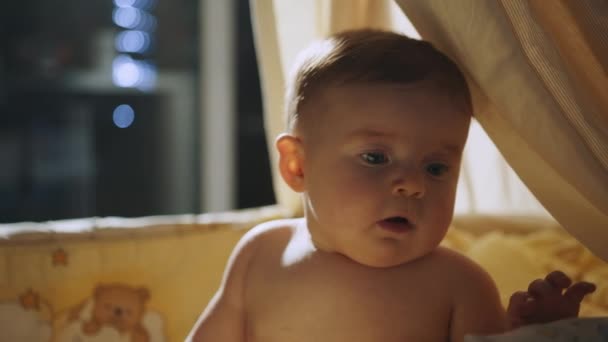 Прикройте следы симпатичного новорожденного, лежащего на спине в детской кроватке. Игровой портрет кавказского новорожденного Тоддлера, смотрящего на вращающиеся игрушки. Концепция детства и родительства. — стоковое видео