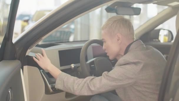 Test driving of new generation electric vehicle with self driving system. Close-up of happy female testing buying car from inside during visit auto dealership. Woman sitting behind the wheel of car — Wideo stockowe