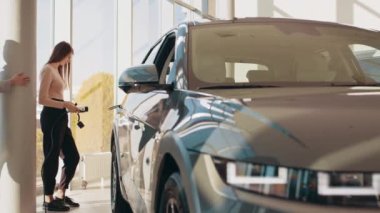 İki mutlu genç kadın ilk defa modern bir kuaför salonunda ya da ofiste elektrikli bir araba şarj ediyorlar. Çevre dostu ulaşım kavramı. Eko elektrikli araba.