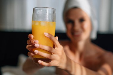 Genç bir kadın modern bir otel dairesinde kahvaltı yapıyor. İş için dizüstü bilgisayar kullanan bornozlu genç bir kızın pencere önü portresi. Yemek ve meyve suyu ile odaklama tepsisi. Serbest Çalışan