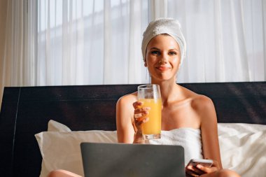 Meyve suyu içip otel odasında dizüstü bilgisayar kullanan bir kadın..