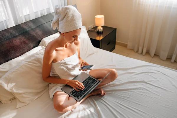 Onnellinen Valkoihoinen Nainen Käyttää Langatonta Kannettavaa Tietokonetta Nukkuessaan Sängyllä Kylpypyyhkeessä — kuvapankkivalokuva