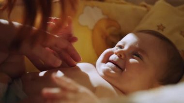 Closeup portrait of a happy baby laughing in crib. Happy family, Mother and child on a bed. Mom and baby are playing. A parent and a small child are resting at home. Family has fun together.