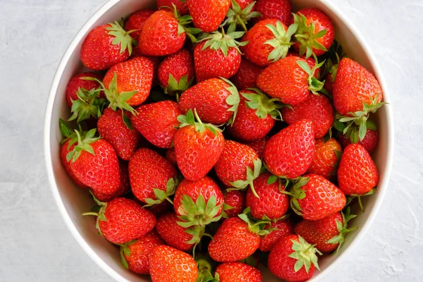 Sulu, parlak ve tatlı çilekler yakın plan beyaz beton bir masada bir kasede.