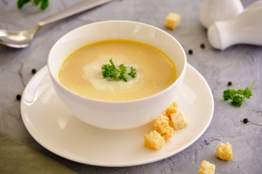 Sebze kremalı çorba, tavuk göğsü ve yeşil arka planda beyaz bir kasede otlar.