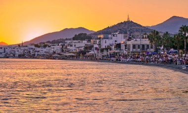 12 Temmuz 2022, Türkiye, Bodrum, şehir plajı. İnsanlar sahildeki masalarda oturup gün batımını seyrediyorlar. Gece manzarası