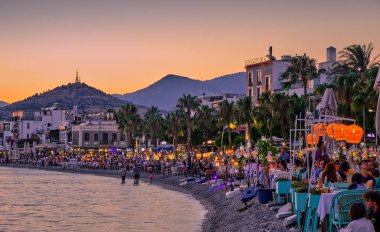 12 Temmuz 2022, Türkiye, Bodrum, şehir plajı. İnsanlar sahildeki masalarda oturup gün batımını seyrediyorlar. Gece manzarası