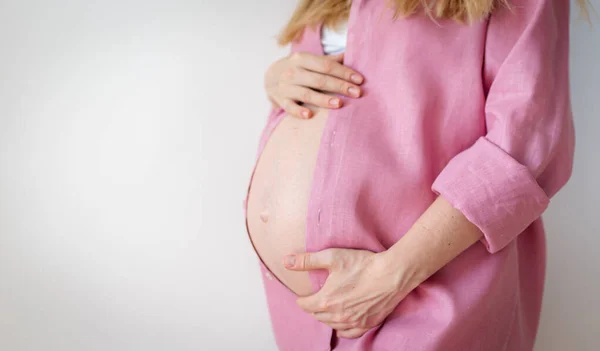 Mulher grávida em uma camisa rosa mantém as mãos na barriga, tecnologia reprodutiva, esperança, novo conceito de vida — Fotografia de Stock