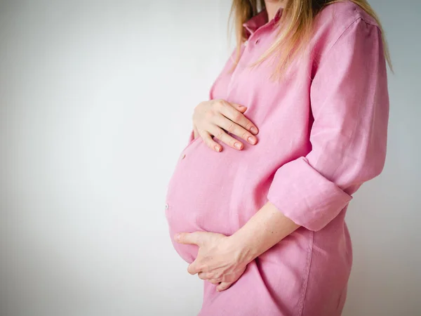 Uma mulher grávida está de pé com as mãos no estômago, o conceito de esperar um bebê — Fotografia de Stock