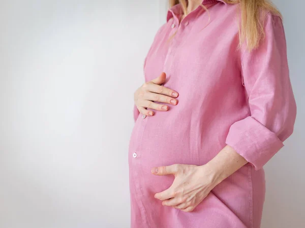 Donna incinta in camicia rosa si erge su uno sfondo bianco — Foto Stock