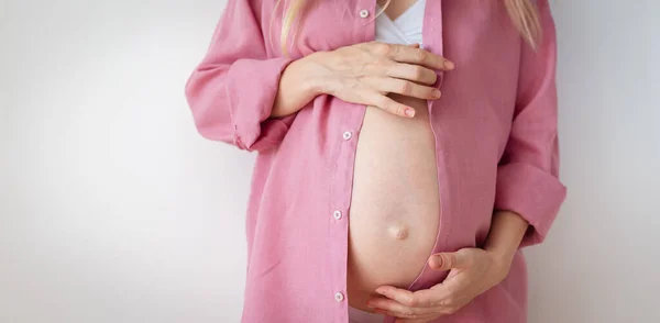 İç çamaşırlı ve pembe gömlekli hamile bir kadın beyaz arka planda duruyor. — Stok fotoğraf