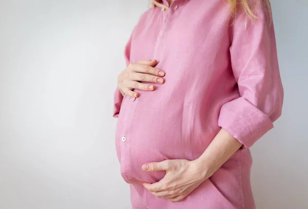 Uma mulher grávida está de pé com as mãos no estômago, o conceito de esperar um bebê — Fotografia de Stock