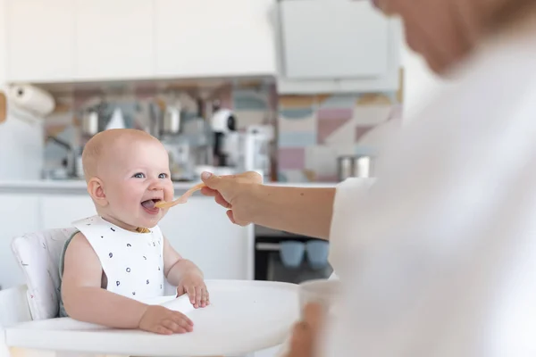 babys first feeding, mom feeds a surprised baby with a spoon. High quality photo