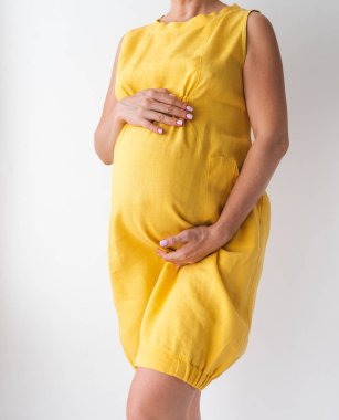 pregnant woman in a yellow dress holds her hands on her stomach on a white background. High quality photo