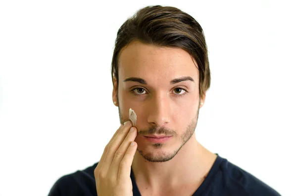 Handsome young man applying moisturizing cream — Stock Photo, Image