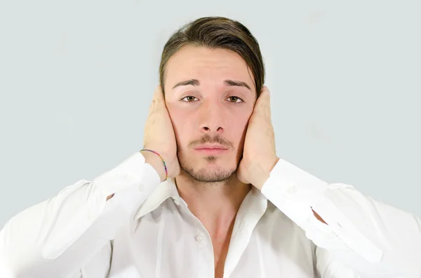 Verdrietig of geïrriteerde jonge man die betrekking hebben op zijn oren met handen — Stockfoto