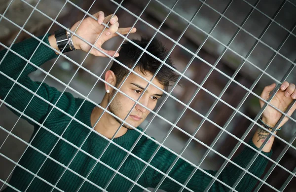 Attractive young man behind metal or steel net — Stock Photo, Image