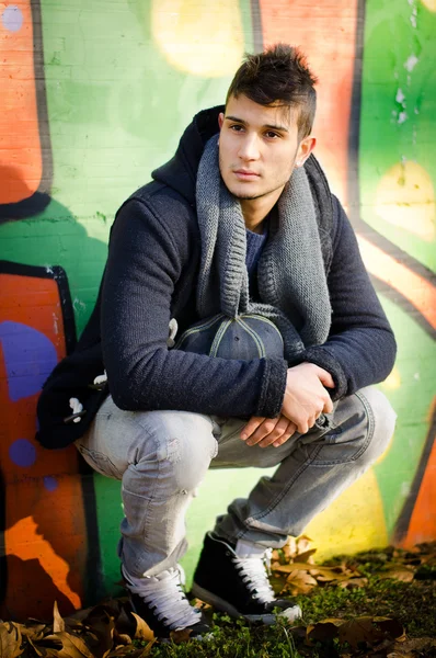 Attractive young man sitting against colorful graffiti — Stock Photo, Image