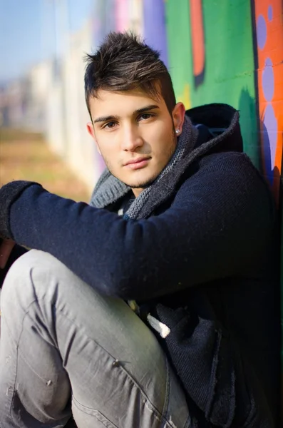 Pohledný mladý muž sedí proti barevné graffiti — Stock fotografie