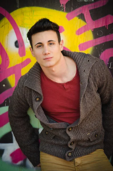 Handsome young man leaning against graffitti wall — Stock Photo, Image