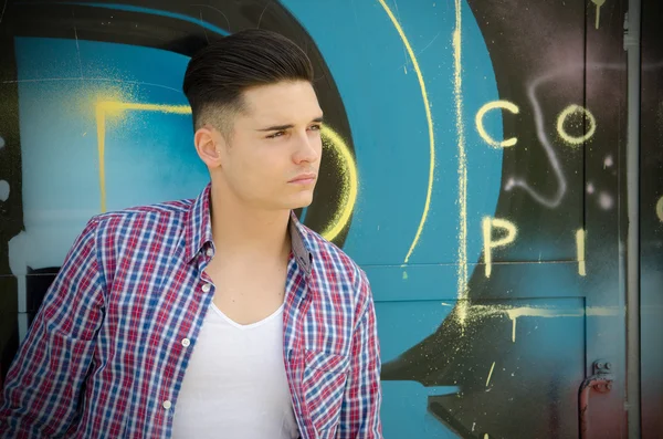 Handsome teenager against colorful graffiti wall — Stock Photo, Image