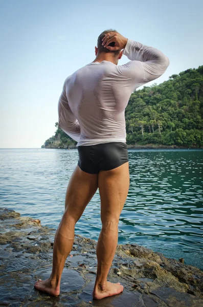 Muscular bodybuilder facing the sea, seen from the back — Stock Photo, Image