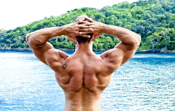 Muscular bodybuilder facing the sea with hands behind his head — Stock Photo, Image