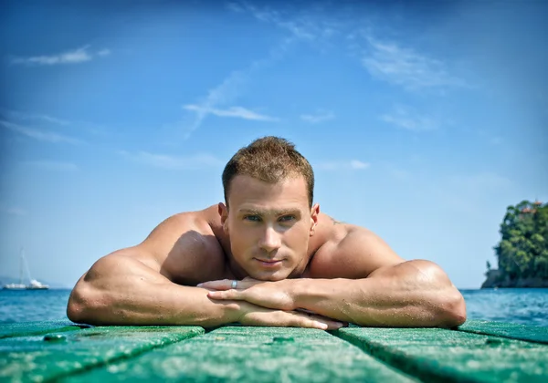 Muscular young man resting his chin on his hands, laying on wood planks — Stock Photo, Image