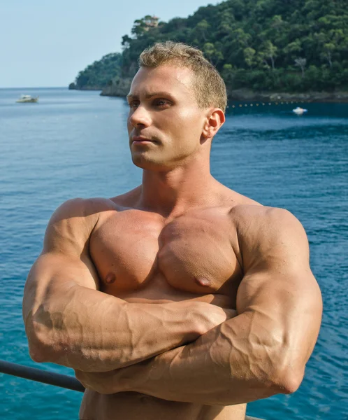 Joven atractivo y muscular fuera frente al mar, los brazos cruzados — Foto de Stock