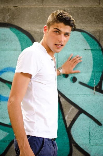 Attractive young man standing in front of graffiti — Stock Photo, Image