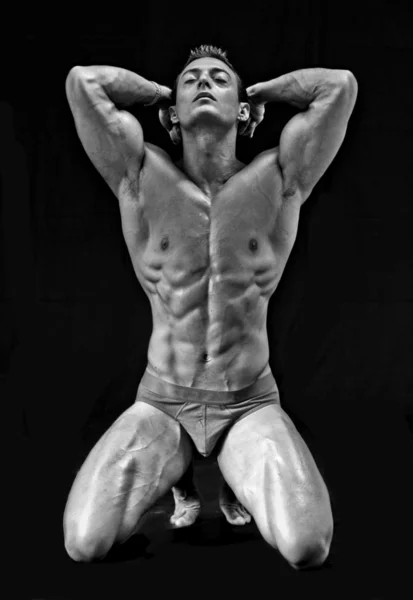 Bianco e nero colpo di bodybuilder giovane inginocchiato, isolato sul nero — Foto Stock