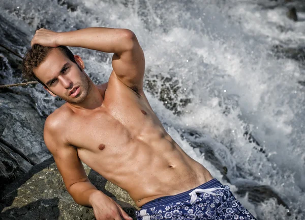 Handsome young man in swimsuit near waterfall — Stock Photo, Image