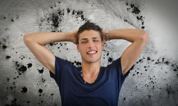 Vacker och självsäker ung man ler, fläckiga väggen bakom honom — Stockfoto