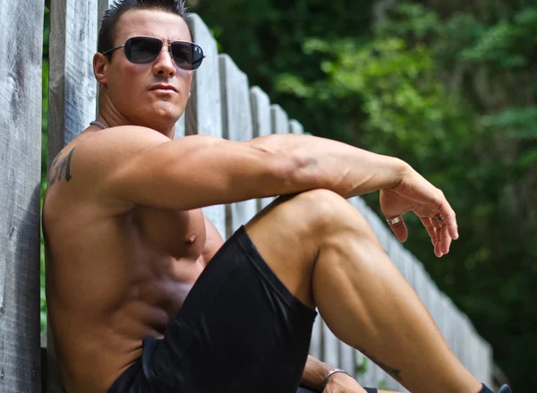 Красивый, серьезный muscleman, сидя против деревянный забор — стоковое фото