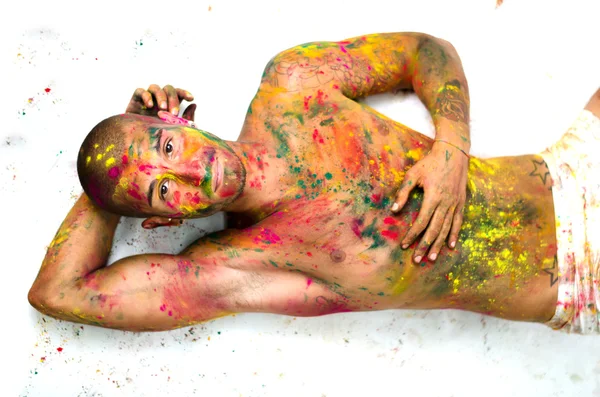 Attractive young man shirtless laying on the floor, skin painted all over with colors — Stock Photo, Image