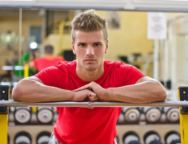 Attractive young man in gym resting on barbell — Stock Photo, Image