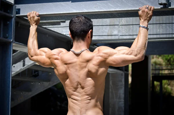 Muscular back of male bodybuilder hanging from metal structure — Stock Photo, Image