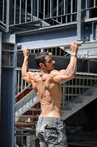 Muscular male bodybuilder seen from back, hanging from metal structure — Stock Photo, Image