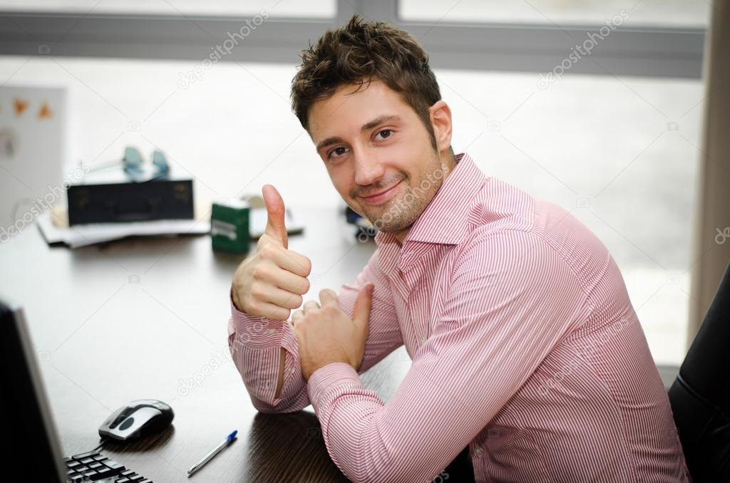 Cheerful office worker at desk doing thumb up sign and smiling