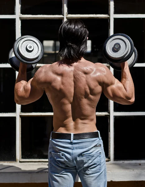 Gespierde jonge bodybuilder shirtless uitwerken, van achteren gezien — Stockfoto