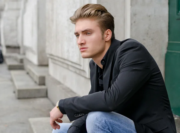 Attraktiv blond junger Mann in Jeans und Jacke, sitzen im freien — Stockfoto