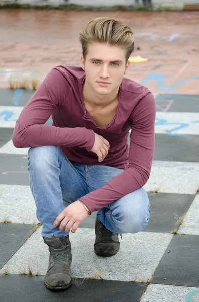 Attractive blue eyed, blond young man sitting on checkered floor — Stock Photo, Image