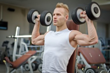 Spor salonunda dambıllarla antrenman yapan çekici bir genç.