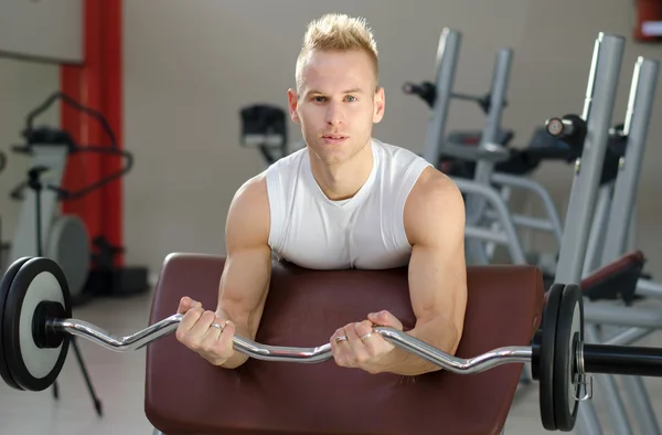 Bonito jovem treinando bíceps no ginásio — Fotografia de Stock