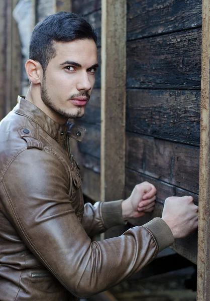 Handsome young man pressing fists on wood planks wall — Stock Photo, Image