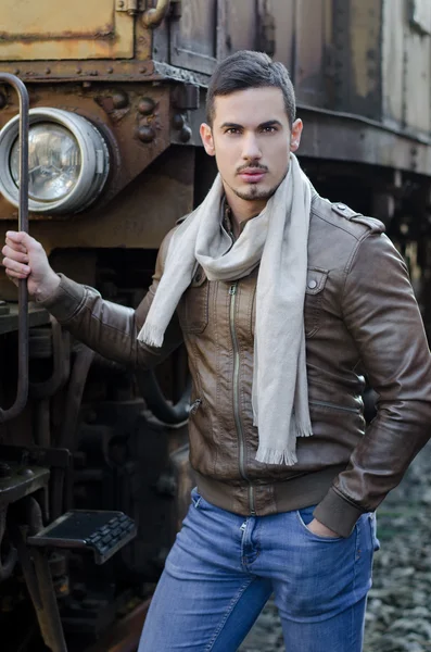 Joven guapo en chaqueta de cuero y jeans junto al tren viejo — Foto de Stock