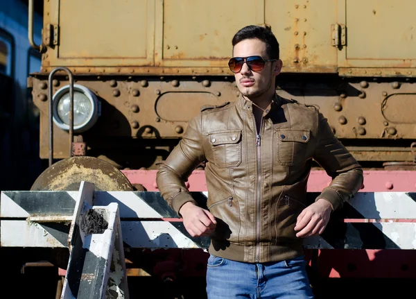 Attractive young man in leather jacket and jeans in front of old train — Stock Photo, Image