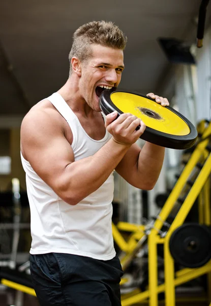 Knappe jongeman bijten groot gewicht schijf in gym — Stockfoto